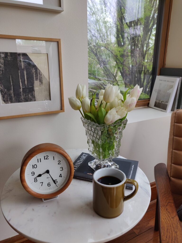 Coffee mug on a table with some flowers and a clock.