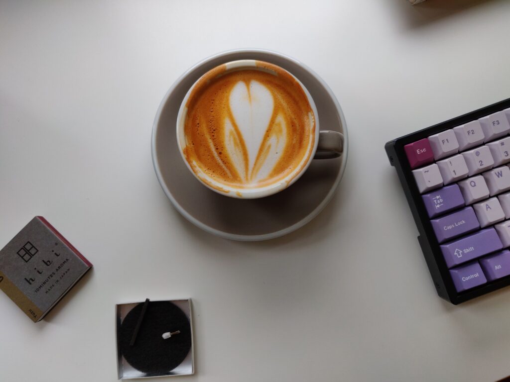 flat white cup with latte art on desk next to keyboard